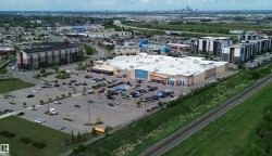Retail complex featuring a large asphalt parking lot, adjacent multi-story residential buildings, and a nearby railway line - 