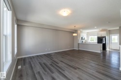 Open-concept living space featuring wood-finish flooring, a kitchen island with seating, white cabinetry, and a black refrigerator - 