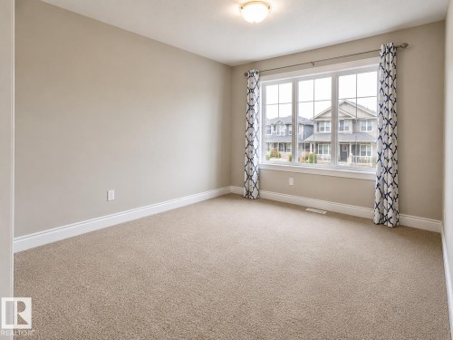 Neutral-toned carpeted room featuring a large window with white trim, a flush mount ceiling light fixture, and light beige wall paint - 7274 Morgan Road, Edmonton, AB 