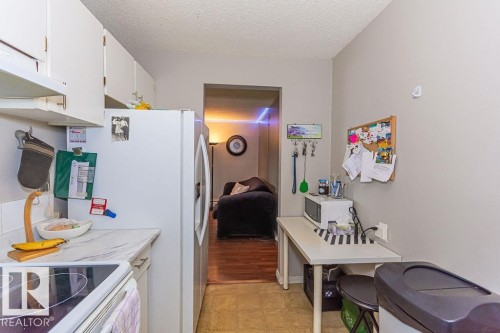 Compact kitchen featuring white cabinetry, a refrigerator, a smooth-top range, and light-colored countertops - 6 3819 76 Street, Edmonton, AB 