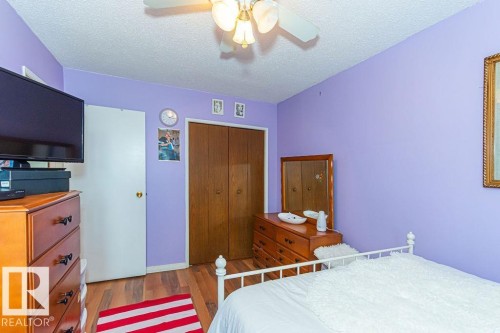 Bedroom featuring wood-finish flooring, a ceiling fan with light fixture, and double-door closet with wood panels - 6 3819 76 Street, Edmonton, AB 