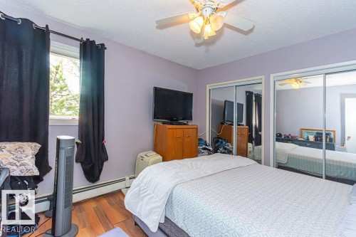 Interior room featuring wood-finish flooring, a ceiling fan with integrated lighting, and two mirrored sliding closet doors - 6 3819 76 Street, Edmonton, AB 
