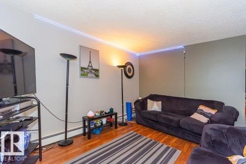 Living area featuring wood-finish flooring, light-toned walls, and a contrasting accent wall - 6 3819 76 Street, Edmonton, AB 