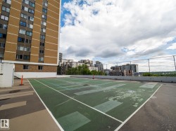 Rooftop tennis court with perimeter fencing, featuring a concrete surface and a partial building facade - 