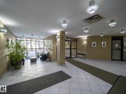 Building lobby featuring white square floor tiles, overhead lighting fixtures, wall-mounted sconces, and a large window wall - 