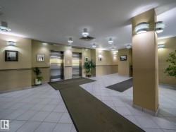 Lobby area featuring two brushed stainless steel elevators, recessed ceiling lighting, wall sconces, and light-toned tile flooring - 
