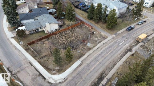 Corner lot featuring a street-facing orientation, mature evergreen trees, a wooden perimeter fence, and concrete sidewalks - 6004 19A Avenue Nw, Edmonton, AB 