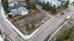 Corner lot featuring a street-facing orientation, mature evergreen trees, a wooden perimeter fence, and concrete sidewalks - 