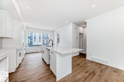 Modern kitchen featuring an island with a breakfast bar, white cabinetry, a black faucet, and wood-finish flooring - #67 5 Rondeau Dr, St. Albert, AB - Indoor Photo Showing Kitchen