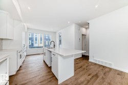 Modern kitchen featuring an island with a breakfast bar, white cabinetry, a black faucet, and wood-finish flooring - 