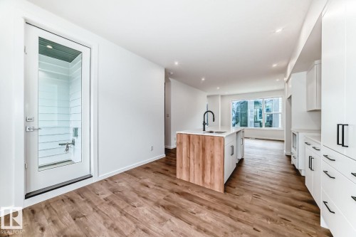 Modern kitchen featuring a central island with wood-finish paneling, white cabinetry, and contrasting matte black hardware - #67 5 Rondeau Dr, St. Albert, AB - Indoor Photo Showing Other Room