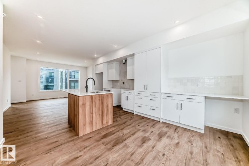 Open-concept living area featuring wood-finish flooring, recessed lighting, and a kitchen island with a built-in sink and matte black faucet - #67 5 Rondeau Dr, St. Albert, AB - Indoor Photo Showing Kitchen