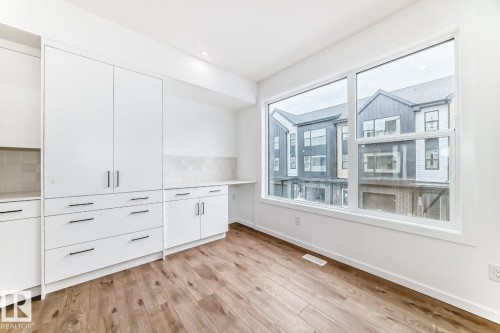 Spacious room featuring wood-finish flooring, a large window, white cabinetry with black hardware, and a light-toned tile backsplash - #67 5 Rondeau Dr, St. Albert, AB - Indoor Photo Showing Other Room