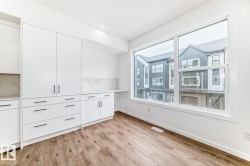 Spacious room featuring wood-finish flooring, a large window, white cabinetry with black hardware, and a light-toned tile backsplash - 