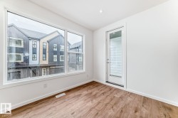 Bright interior space featuring a large picture window, a separate glass-paneled door, recessed ceiling lighting, wood-finish flooring, and crisp white baseboards - 