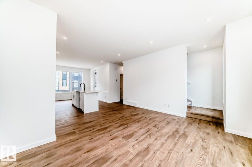Open-concept living space featuring wood-finish flooring, recessed lighting, white walls, and a contemporary kitchen island with a black faucet - #67 5 Rondeau Dr, St. Albert, AB - Indoor