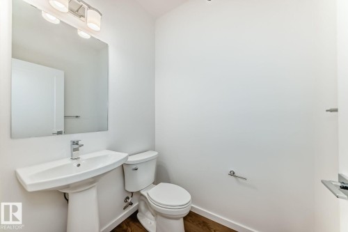 Powder room featuring a pedestal sink with a chrome faucet, a rectangular wall-mounted mirror, and a three-light vanity fixture - #67 5 Rondeau Dr, St. Albert, AB - Indoor Photo Showing Bathroom