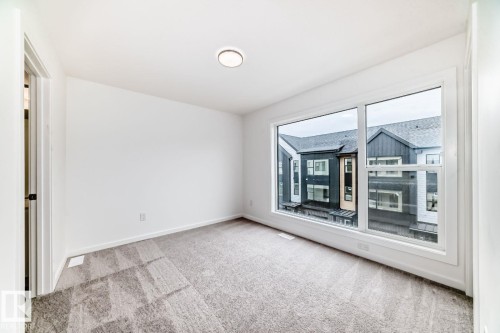 Spacious interior with neutral-toned carpeting, white walls, and a large window offering ample natural light - #67 5 Rondeau Dr, St. Albert, AB - Indoor Photo Showing Other Room
