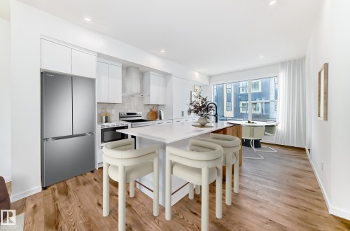 Modern kitchen featuring white cabinetry, stainless steel appliances, a white island countertop, and wood-finish flooring - #67 5 Rondeau Dr, St. Albert, AB - Indoor