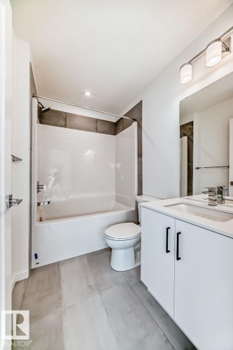 Contemporary bathroom featuring a white vanity with black hardware, a rectangular undermount sink, and a white bathtub with a tile surround - #67 5 Rondeau Dr, St. Albert, AB - Indoor Photo Showing Bathroom