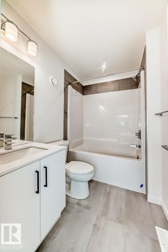 Bathroom featuring a white vanity with matte black hardware, a matching white toilet, and a bathtub with a tiled surround - #67 5 Rondeau Dr, St. Albert, AB - Indoor Photo Showing Bathroom