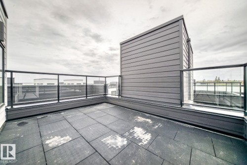 Rooftop patio featuring large format tile flooring, clear glass railing, and dark horizontal siding - #67 5 Rondeau Dr, St. Albert, AB - 