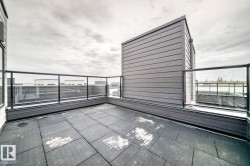 Rooftop patio featuring large format tile flooring, clear glass railing, and dark horizontal siding - 