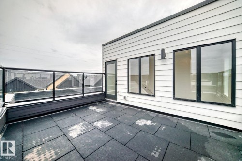 Rooftop deck featuring large format pavers, a glass and metal railing system, white horizontal siding, black-framed windows, and a black exterior door - #67 5 Rondeau Dr, St. Albert, AB - Outdoor With Exterior