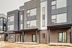 Modern townhome exterior featuring multi-level architecture, large picture windows, and a mix of dark gray siding with vertical corrugated metal accents - 