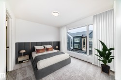 Bright bedroom featuring a large picture window, light-colored carpeting, a contemporary flush-mount ceiling light, and a built-in upholstered headboard - 