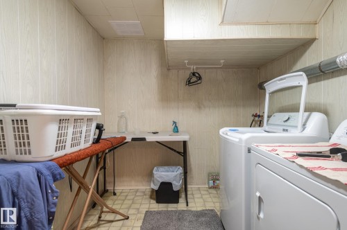 Laundry area featuring a top-load washing machine, a front-load dryer, wood-panel walls, and light-colored square tile flooring - 13816 62 Street, Edmonton, AB 