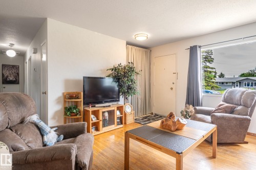 Living area with wood-finish flooring, a large window, and a white entry door - 13816 62 Street, Edmonton, AB 