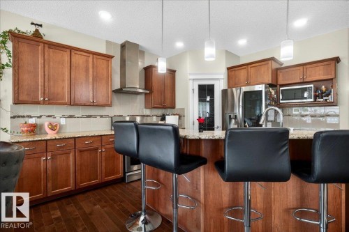 Kitchen featuring wood-finish cabinetry, stainless steel appliances, granite countertops, a tiled backsplash, and pendant lighting over a breakfast bar - 1411 30 Avenue, Edmonton, AB 