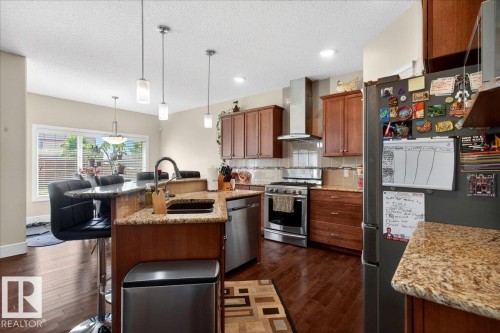 Kitchen featuring wood-finish flooring, granite countertops, stainless steel appliances, pendant lighting, and wood cabinetry - 1411 30 Avenue, Edmonton, AB 