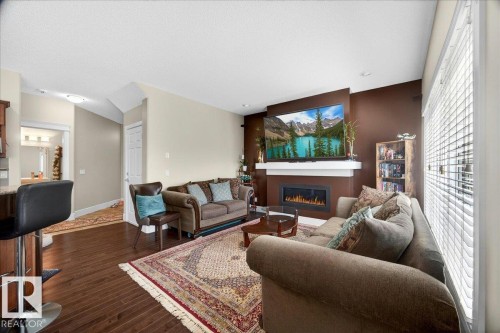 Spacious living area featuring rich wood-finish flooring, a contemporary linear fireplace with a mantle, and a large window with white blinds - 1411 30 Avenue, Edmonton, AB 
