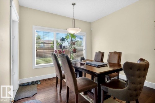 Dining area featuring wood-finish flooring, a large window with horizontal blinds, neutral wall paint, white baseboards, and a contemporary pendant light fixture - 1411 30 Avenue, Edmonton, AB 