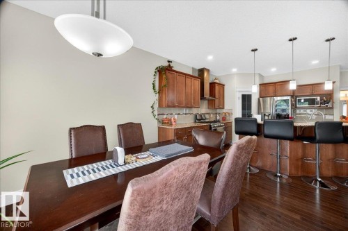 Open-concept kitchen and dining area featuring wood-finish flooring, wood cabinetry, stainless steel appliances, and a kitchen island with pendant lighting - 1411 30 Avenue, Edmonton, AB 