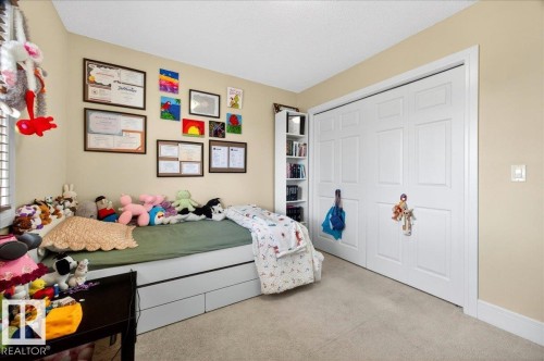 Bedroom featuring light beige wall color, light-colored carpet flooring, white bi-fold closet doors, white baseboards, and a built-in white shelving unit - 1411 30 Avenue, Edmonton, AB 
