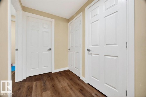 Interior hallway featuring dark wood-finish flooring, light beige wall paint, and multiple white panel doors with brushed nickel hardware - 1411 30 Avenue, Edmonton, AB 