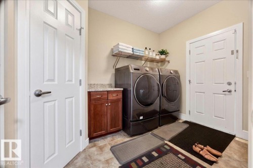 Laundry area featuring light-toned wall paint, tiled flooring, wood cabinetry with a light-toned countertop, and white paneled doors - 1411 30 Avenue, Edmonton, AB 