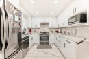 Modern kitchen featuring white high-gloss cabinetry with bar pull hardware, integrated stainless steel appliances, and a U-shaped countertop with a matching backsplash - 3843 47 Street, Edmonton, AB 