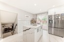 Contemporary kitchen featuring a central island with a waterfall countertop and integrated storage, stainless steel refrigerator, white gloss cabinetry, and large format porcelain tile flooring - 3843 47 Street, Edmonton, AB 