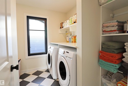 Dedicated laundry area featuring checkerboard flooring, a window with black trim, built-in shelving, and a countertop space - 100 Graybriar Drive, Stony Plain, AB - Indoor Photo Showing Laundry Room