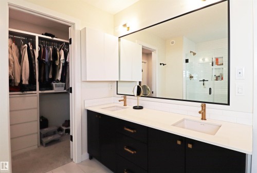 Bathroom vanity with dual undermount sinks, bronze-finish faucets, and white quartz countertop with access to walk-in closet and laundry room. - 100 Graybriar Drive, Stony Plain, AB - Indoor Photo Showing Other Room