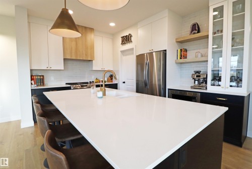 Modern kitchen featuring a large central island with quartz countertop, brass-finish faucet, undermount sink, beverage nook, stainless appliances and a walk-through pantry - 100 Graybriar Drive, Stony Plain, AB - Indoor Photo Showing Kitchen With Upgraded Kitchen