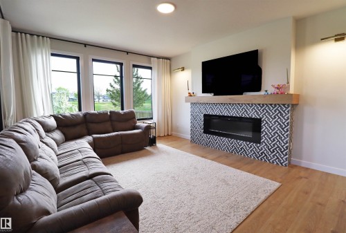 Living area featuring a geometric-patterned fireplace surround with a wood mantle, an inset linear electric fireplace with plenty of natural light and an unobstructed view of the backyard and golf course. - 100 Graybriar Drive, Stony Plain, AB - Indoor Photo Showing Living Room With Fireplace