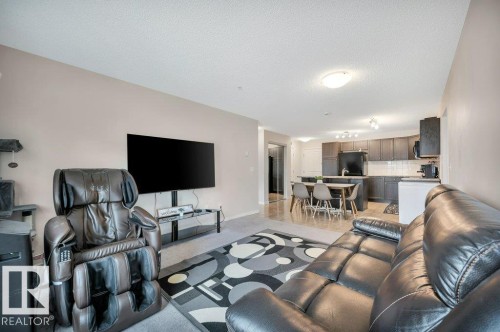 Open-concept living space featuring neutral wall tones, recessed lighting, and a kitchen with dark cabinetry, white subway tile backsplash, and a breakfast bar - 219 1820 Rutherford Road, Edmonton, AB 