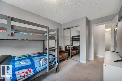 Carpeted bedroom with grey walls, white baseboards, mirrored closet doors, and an open doorway - 219 1820 Rutherford Road, Edmonton, AB 