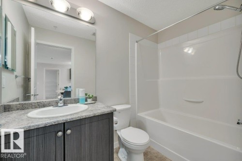 Full bathroom featuring a single vanity with wood-finish cabinetry, a white oval sink, and a speckled countertop - 219 1820 Rutherford Road, Edmonton, AB 