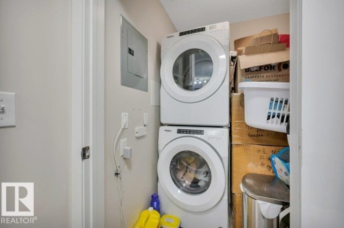 Dedicated laundry closet featuring a stacked white front-loading washer and dryer, an electrical panel, and light-toned wall paint - 219 1820 Rutherford Road, Edmonton, AB 